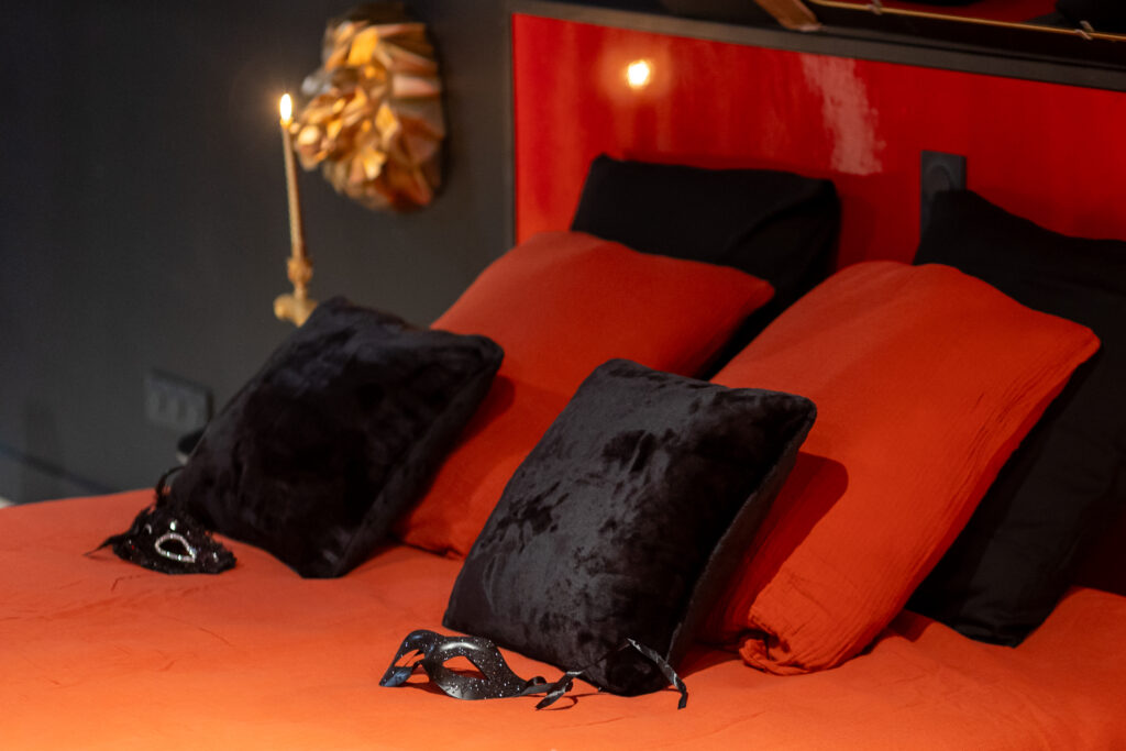 lit king size avec cousins rouge et noir et masque posé dessus